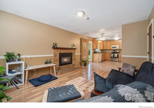 living area featuring a ceiling fan, light wood-type flooring, a brick fireplace, and a textured ceiling