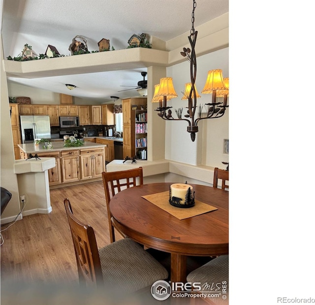 dining space featuring ceiling fan with notable chandelier, vaulted ceiling, a textured ceiling, and light wood-type flooring