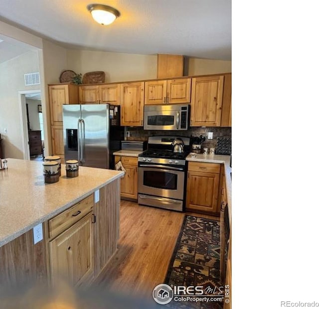 kitchen with stainless steel appliances, vaulted ceiling, light hardwood / wood-style floors, and backsplash