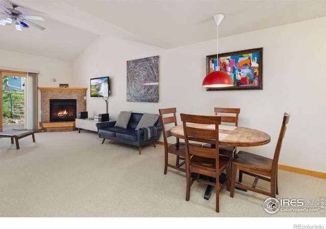 carpeted dining space with a ceiling fan, lofted ceiling, baseboards, and a tile fireplace