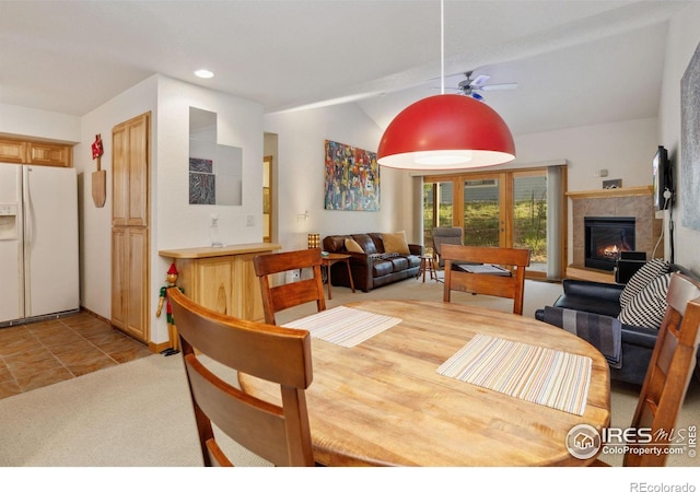 dining room featuring ceiling fan, lofted ceiling, light tile patterned flooring, a tile fireplace, and light carpet