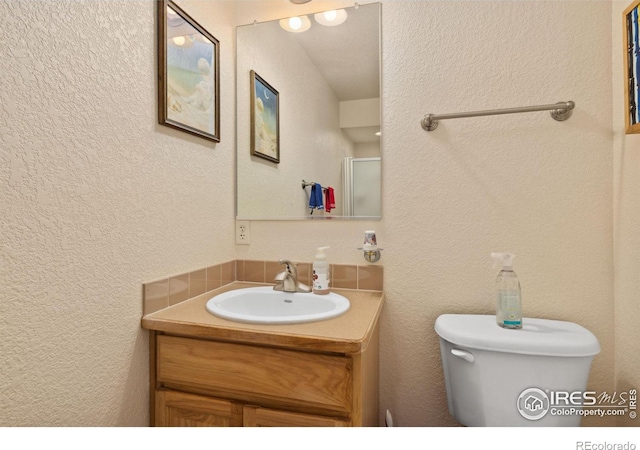 bathroom featuring toilet, a textured wall, and vanity