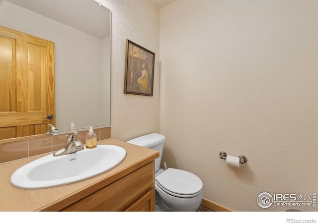 bathroom with a textured wall, vanity, and toilet