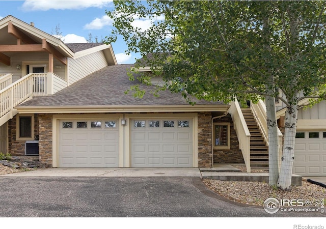 view of front of home featuring a garage, a shingled roof, stairs, driveway, and stone siding