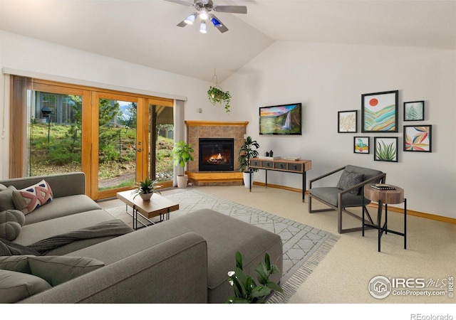 living area with light colored carpet, a tiled fireplace, vaulted ceiling, ceiling fan, and baseboards