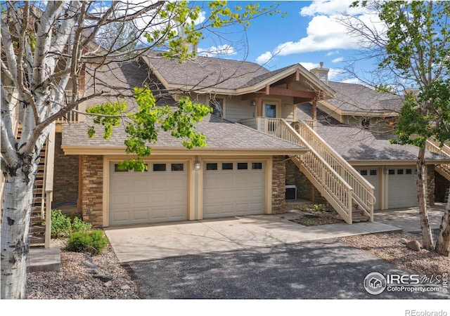 view of front of home featuring driveway, stone siding, a chimney, roof with shingles, and stairs