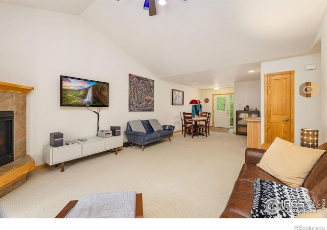 living area with ceiling fan, high vaulted ceiling, a tiled fireplace, and carpet flooring