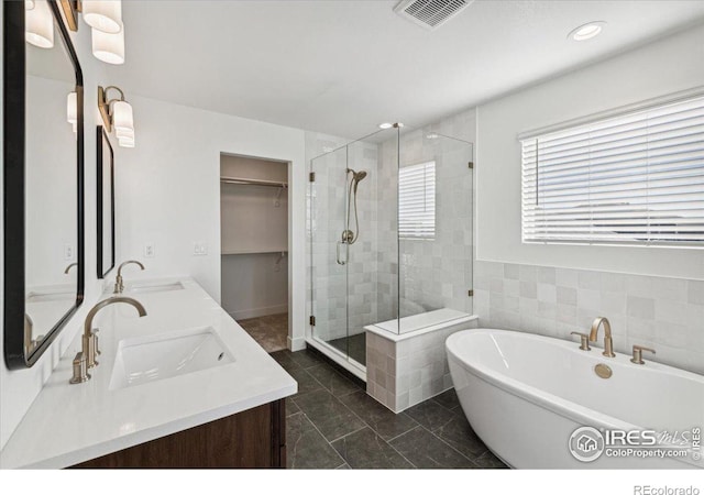 bathroom featuring plus walk in shower, vanity, tile walls, and tile patterned flooring