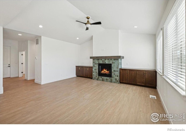 unfurnished living room with ceiling fan, light hardwood / wood-style floors, a tile fireplace, and vaulted ceiling