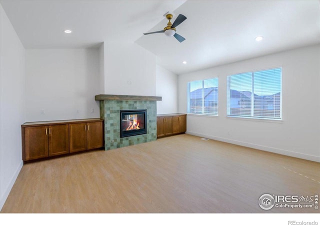 unfurnished living room featuring light hardwood / wood-style floors, ceiling fan, lofted ceiling, and a tiled fireplace