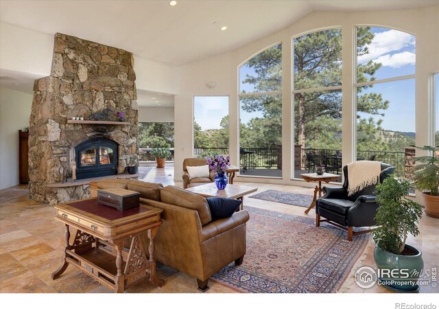 living room with a wealth of natural light, a stone fireplace, tile floors, and lofted ceiling