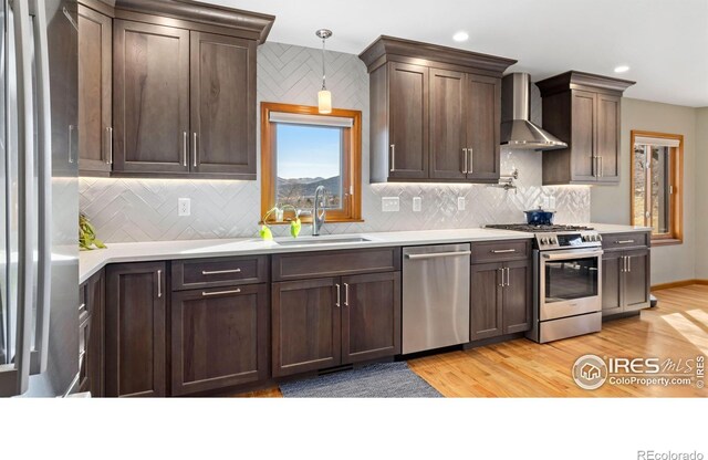 kitchen featuring appliances with stainless steel finishes, light wood-type flooring, wall chimney exhaust hood, and decorative backsplash