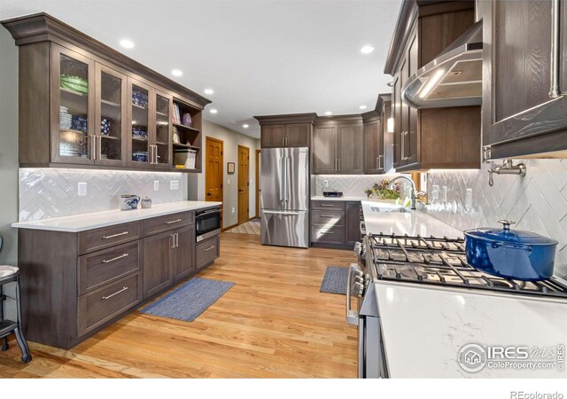 kitchen with appliances with stainless steel finishes, backsplash, light wood-type flooring, and wall chimney exhaust hood