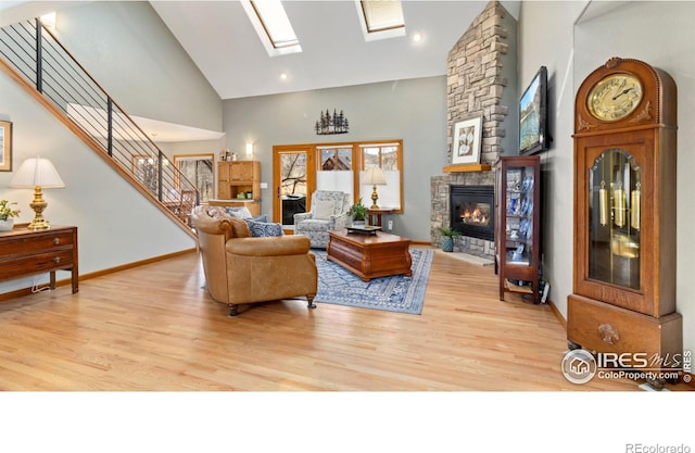 living room with a skylight, a stone fireplace, high vaulted ceiling, and light hardwood / wood-style floors