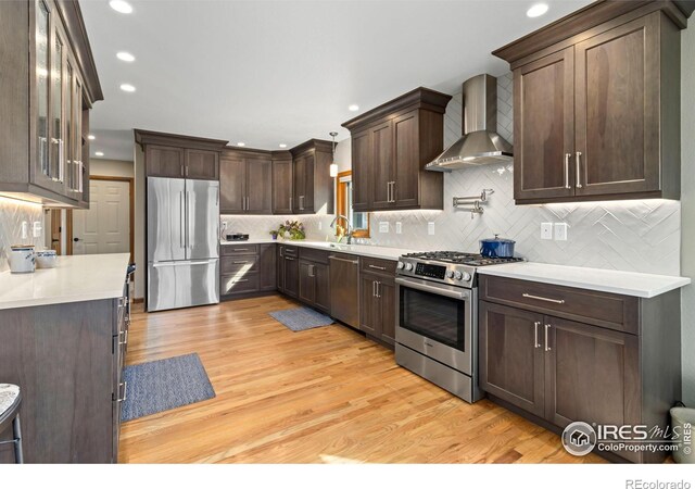 kitchen featuring light hardwood / wood-style flooring, stainless steel appliances, wall chimney exhaust hood, and backsplash