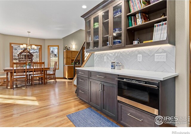 kitchen with light hardwood / wood-style flooring, a chandelier, oven, hanging light fixtures, and backsplash