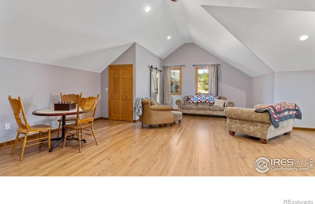 interior space featuring a barn door, light wood-type flooring, and vaulted ceiling