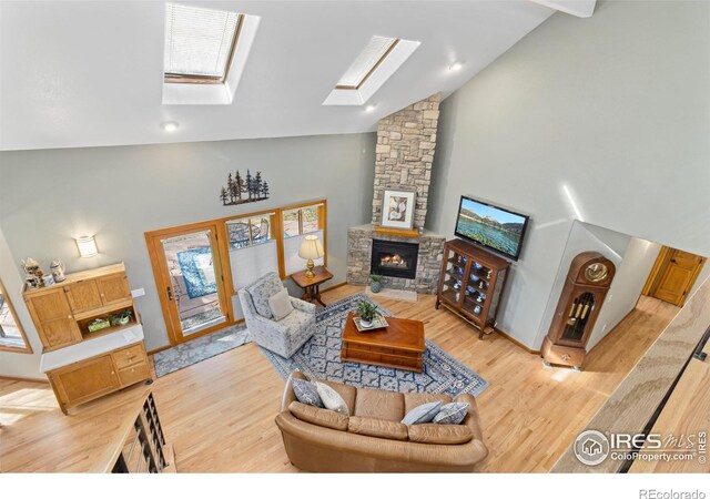 living room with high vaulted ceiling, light wood-type flooring, a skylight, and a fireplace