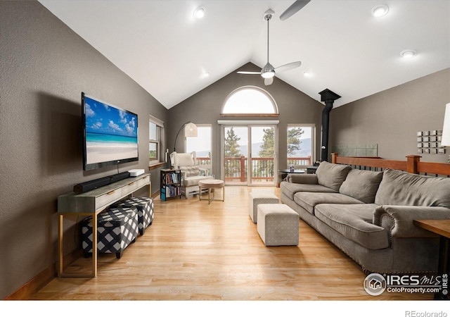 living room featuring ceiling fan, high vaulted ceiling, a wood stove, and light wood-type flooring