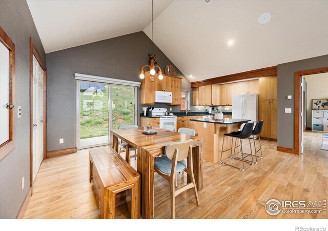 kitchen with pendant lighting, high vaulted ceiling, white appliances, and light hardwood / wood-style floors