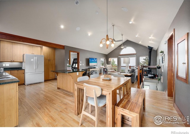 dining room featuring an inviting chandelier, high vaulted ceiling, light wood-type flooring, and a wood stove