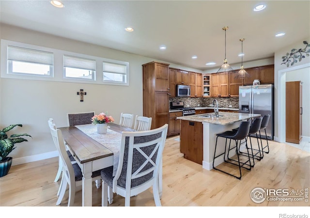 kitchen featuring light stone countertops, hanging light fixtures, backsplash, appliances with stainless steel finishes, and light wood-type flooring