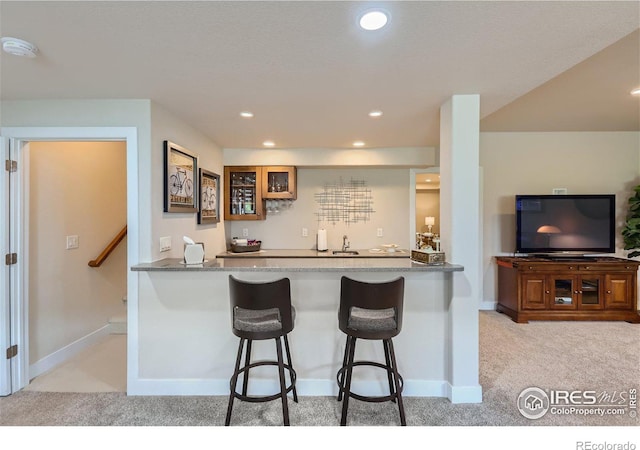 kitchen featuring a kitchen bar, kitchen peninsula, light colored carpet, and light stone counters