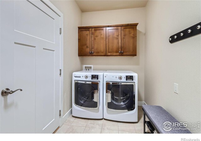 washroom featuring washing machine and clothes dryer, light tile patterned floors, and cabinets