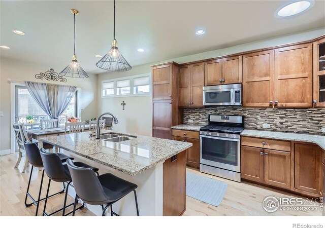 kitchen with a kitchen breakfast bar, sink, decorative backsplash, light stone countertops, and appliances with stainless steel finishes