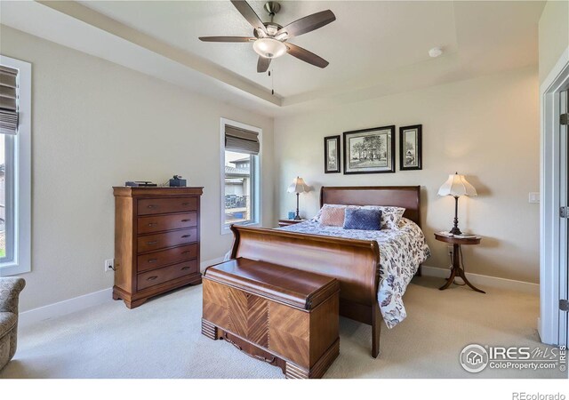 bedroom featuring light carpet, a tray ceiling, and ceiling fan