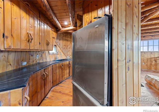 kitchen with stainless steel refrigerator, sink, light hardwood / wood-style flooring, wood walls, and wood ceiling