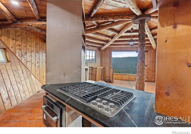 kitchen with wooden ceiling, wall oven, wood walls, wood-type flooring, and stainless steel gas stovetop