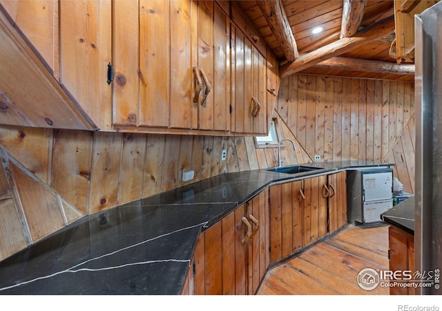 kitchen with beam ceiling, sink, light hardwood / wood-style floors, wooden walls, and wood ceiling