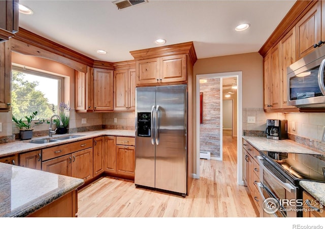 kitchen with sink, decorative backsplash, light stone countertops, appliances with stainless steel finishes, and light hardwood / wood-style floors