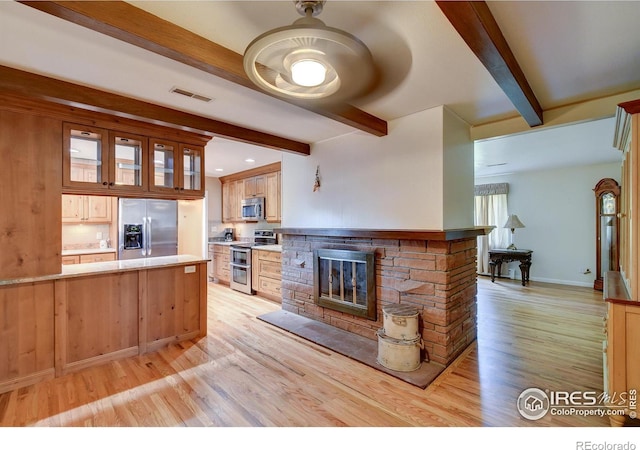 kitchen featuring kitchen peninsula, light wood-type flooring, stainless steel appliances, beamed ceiling, and a stone fireplace