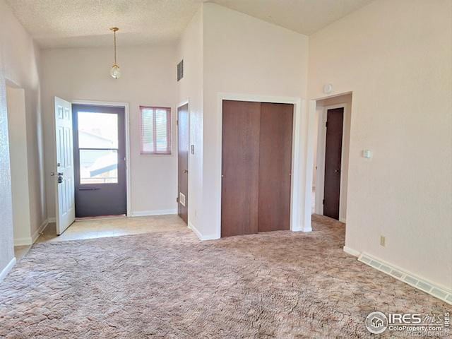 foyer entrance featuring light carpet, high vaulted ceiling, and a textured ceiling