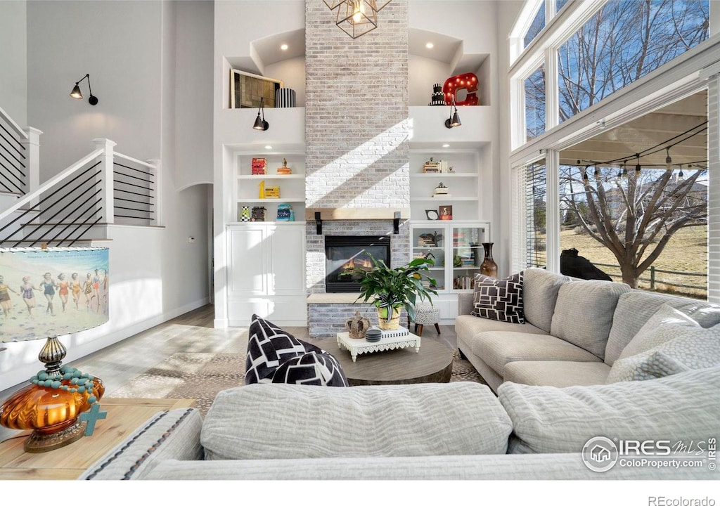 living room with wood-type flooring, a fireplace, a towering ceiling, and built in shelves