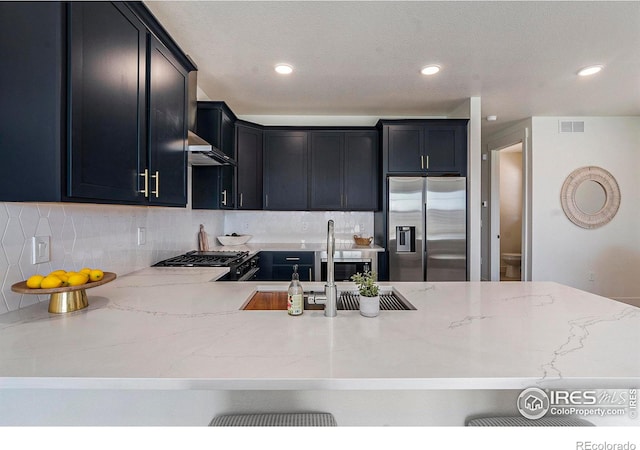 kitchen featuring light stone counters, backsplash, stainless steel fridge, exhaust hood, and range