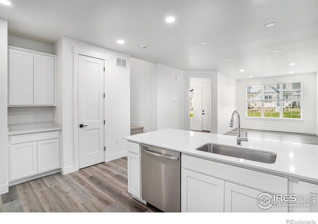 kitchen with light hardwood / wood-style flooring, sink, stainless steel dishwasher, white cabinetry, and a textured ceiling