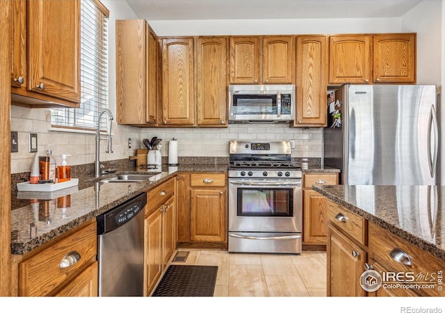 kitchen with sink, stainless steel appliances, backsplash, and dark stone countertops