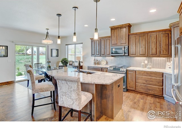 kitchen featuring stainless steel appliances, light stone counters, hanging light fixtures, and a kitchen island with sink