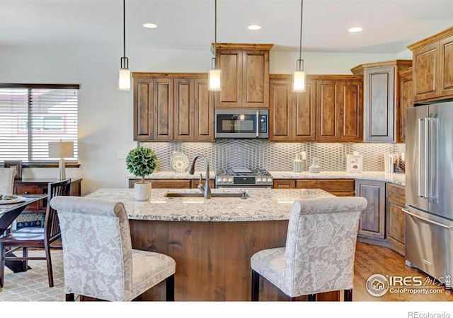 kitchen with an island with sink, decorative light fixtures, light stone countertops, stainless steel appliances, and a sink