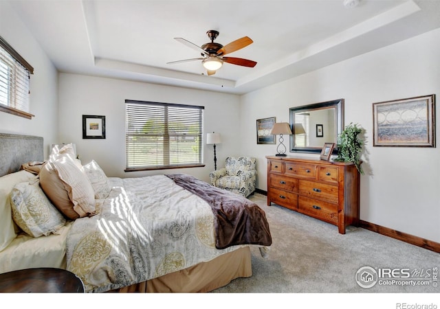 bedroom featuring multiple windows, baseboards, a raised ceiling, and light colored carpet