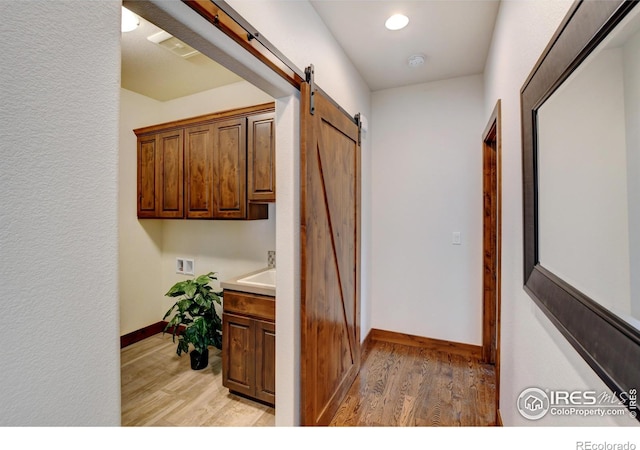 hall featuring light wood finished floors, a barn door, baseboards, and recessed lighting