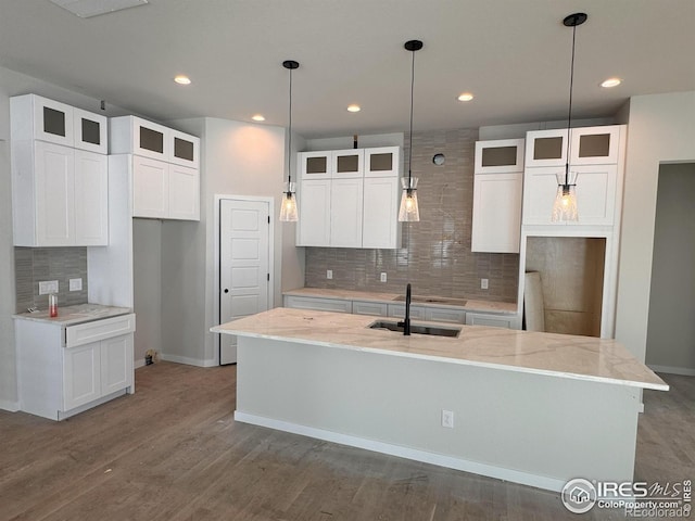 kitchen with white cabinets, a center island with sink, light stone counters, and sink