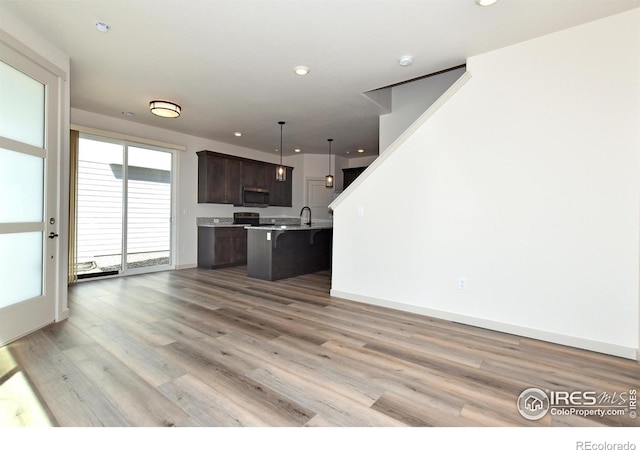 kitchen featuring a kitchen bar, light hardwood / wood-style flooring, dark brown cabinets, a center island with sink, and pendant lighting