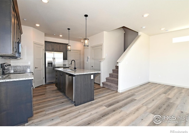 kitchen featuring sink, light stone counters, decorative light fixtures, a center island with sink, and stainless steel appliances