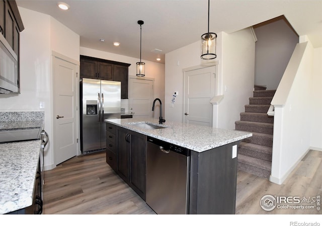 kitchen featuring appliances with stainless steel finishes, decorative light fixtures, sink, a kitchen island with sink, and light hardwood / wood-style flooring