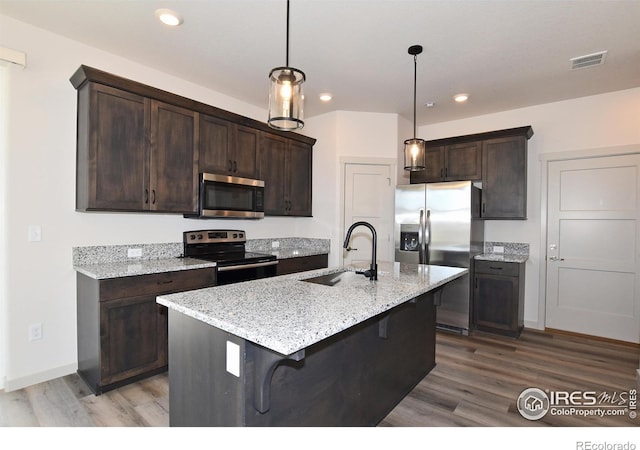 kitchen featuring dark brown cabinetry, sink, light stone counters, appliances with stainless steel finishes, and an island with sink