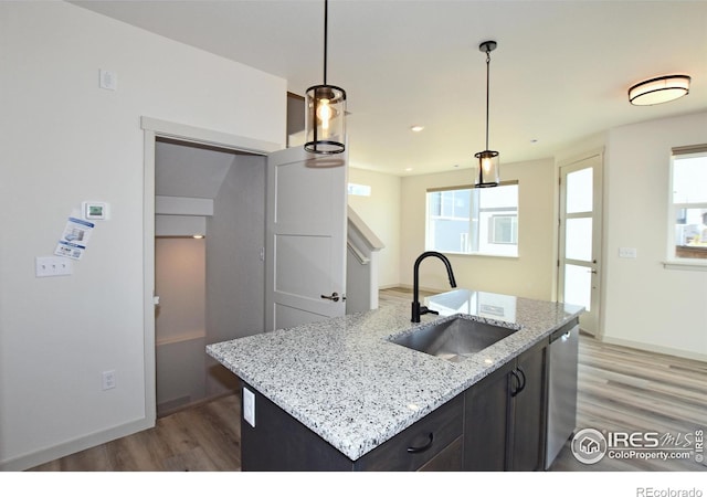 kitchen featuring sink, light stone counters, hanging light fixtures, a center island with sink, and hardwood / wood-style floors